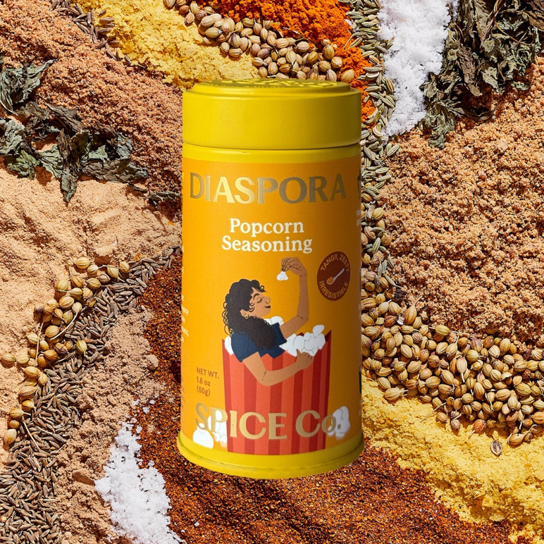 una lata de condimento para palomitas de maíz de Diaspora Co. superpuesta a una mezcla de especias