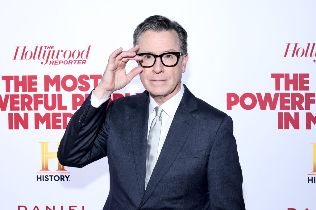 Stephen Colbert con traje y gafas en la mano