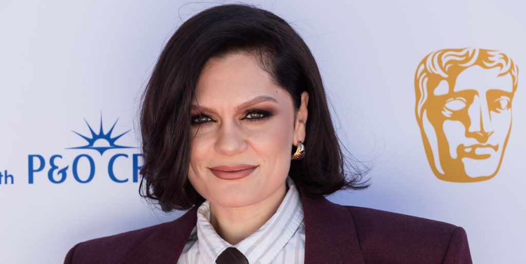 Jessie J on the BAFTA red carpet in 2025 wearing a pin-striped shirt, tie and burgundy blazer.
