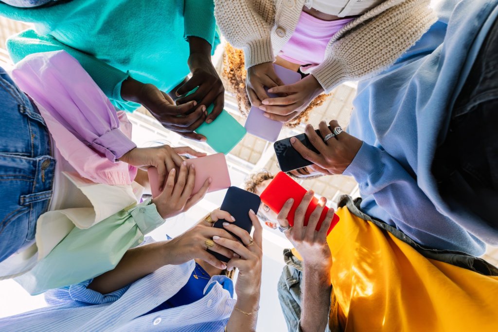 Vista de ángulo bajo de un grupo de jóvenes con dispositivos móviles en las calles de la ciudad. Diversos amigos adolescentes adictos viendo contenido de redes sociales en aplicaciones para teléfonos inteligentes. Juventud, gente tecnológica y concepto de estilo de vida tecnológico.
