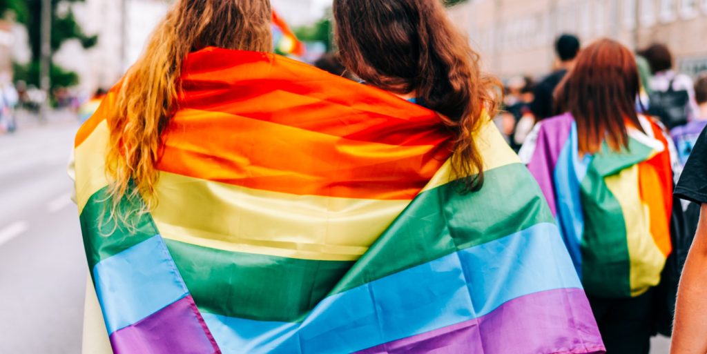 Two women wearing an LGBTQ+ Pride flag