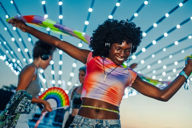 Una joven feliz bailando con amigos en un festival de música al aire libre, usando audífonos y una bufanda colorida, disfrutando de la atmósfera vibrante bajo luces centelleantes