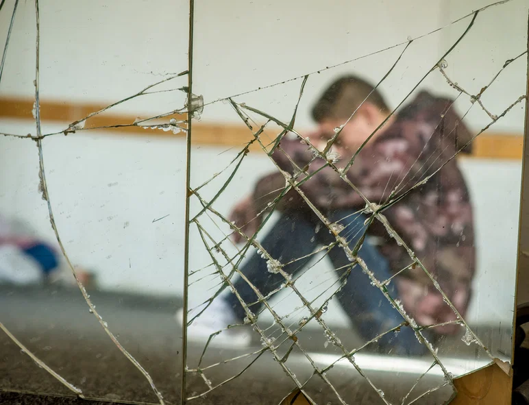 Joven sentado deprimido, reflejado en un espejo roto