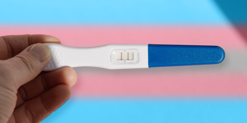 person holding a pregnancy test over trans flag colours