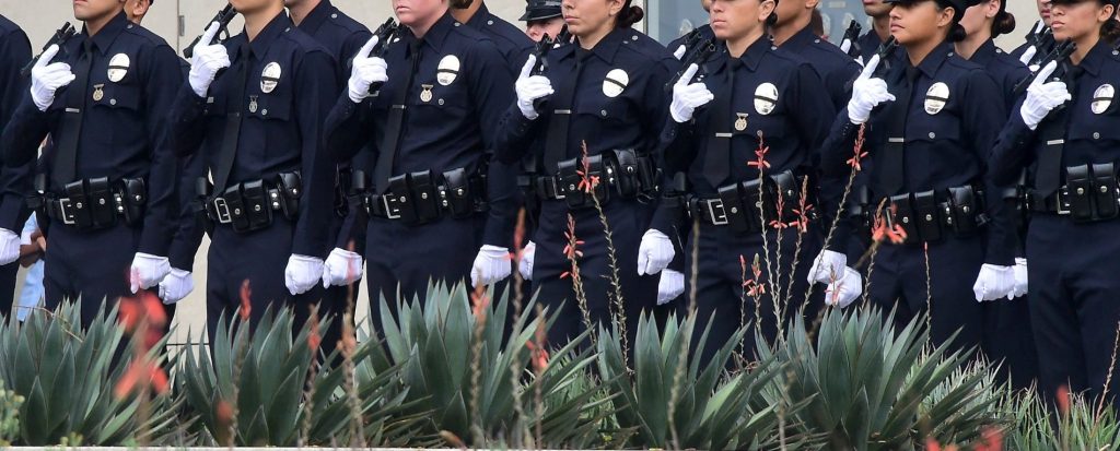 With black ribbons across their badge and holding a gun, police recruits attend their graduation ceremony at LAPD Headquarters
